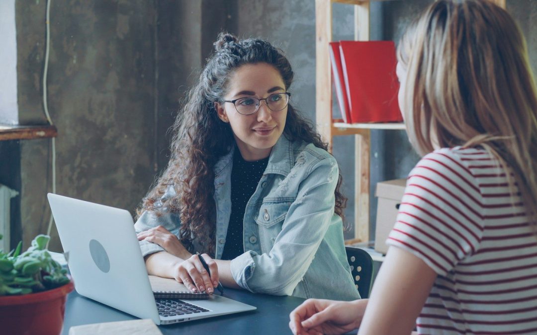Two women are having a conversation at a desk